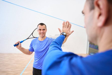 Foto de Squash jugadores hombre con raquetas dando alta cinco mirándose el uno al otro en la cancha de interior - Imagen libre de derechos
