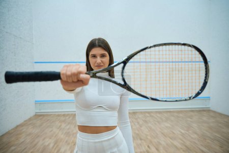 Foto de Deportiva mujer segura en pista de squash mostrando raqueta - Imagen libre de derechos