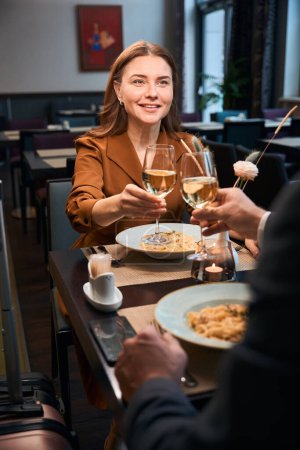 Foto de Adulto sonriente mujer caucásica y hombre recortado tostando vino de copas en el restaurante del hotel. Concepto de fecha y evento romántico - Imagen libre de derechos