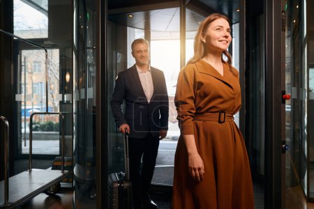 Photo for Smiling adult caucasian couple with suitcases entering to hotel lobby at daytime. Concept of rest, vacation and travelling - Royalty Free Image
