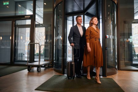 Téléchargez les photos : Couple caucasien adulte avec valises entrant dans le hall de l'hôtel par une journée ensoleillée. Concept de repos, vacances et voyages - en image libre de droit
