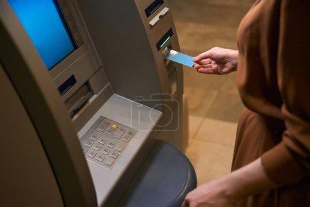 Téléchargez les photos : Image recadrée de la femme insérez une carte de crédit dans le guichet automatique dans le hall de l'hôtel. Concept de repos, vacances et voyages - en image libre de droit