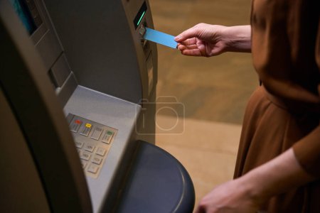Téléchargez les photos : Image partielle de la femme insérer une carte de crédit dans le guichet automatique dans le hall de l'hôtel. Concept de repos, vacances et voyages - en image libre de droit