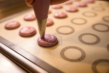 Foto de Primer plano de la mano que aprieta la masa de macaron de la bolsa de pastelería en la estera de hornear de silicona - Imagen libre de derechos