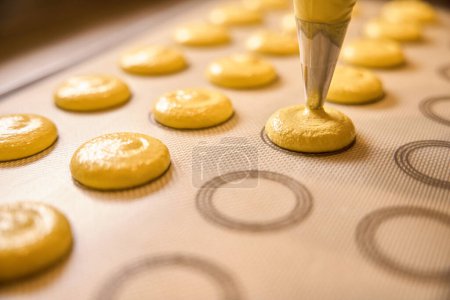 Foto de Primer plano de la masa de limón macaron que se exprime a través de la punta de la bolsa de pastelería en la estera de hornear de silicona - Imagen libre de derechos