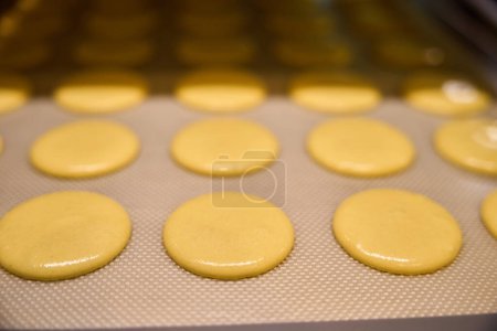 Foto de Primer plano de las cáscaras de macarón limón brillante colocado en la estera de silicona en la bandeja de la hoja - Imagen libre de derechos