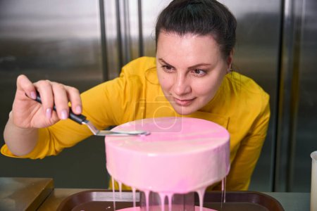 Téléchargez les photos : Chef pâtissier concentré étalant la couche de glaçage sur le dessus du gâteau à l'aide d'une spatule - en image libre de droit