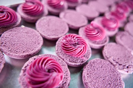 Foto de Primer plano de conchas de macaron púrpura con relleno de crema en bandeja de hoja colocada en la encimera de la cocina - Imagen libre de derechos