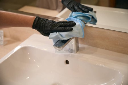 Photo for Cropped photo of female hand in disposable nitrile glove wiping faucet with microfiber cloth - Royalty Free Image
