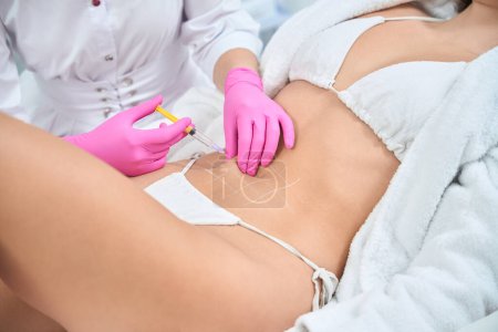 Photo for Beautician holding white pencil and marking zones on belly before beauty procedure in professional salon - Royalty Free Image