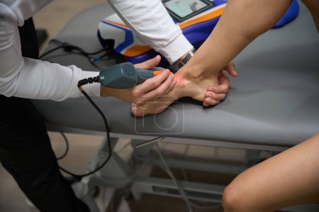 Téléchargez les photos : Photo rapprochée de la femme faisant l'objet d'une thérapie laser pour réduire l'enflure et l'inflammation à pied - en image libre de droit
