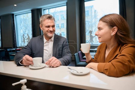Photo for Smiling man and lady drinking coffee while sitting at bar counter in restaurant - Royalty Free Image