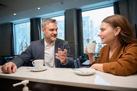 Photo for Men telling something and lady listening to him while drinking coffee at bar counter in cafe - Royalty Free Image