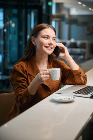 Téléchargez les photos : Photo rapprochée de dame joyeuse parlant au téléphone et buvant du café tout en étant assis au café - en image libre de droit