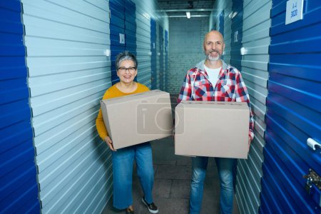 Foto de Dos personas de pie con cajas llenas de cosas en el pasillo de un trastero - Imagen libre de derechos