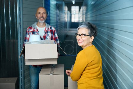 Photo for Lady with a short haircut looks at the camera while a man carries a box of things. - Royalty Free Image