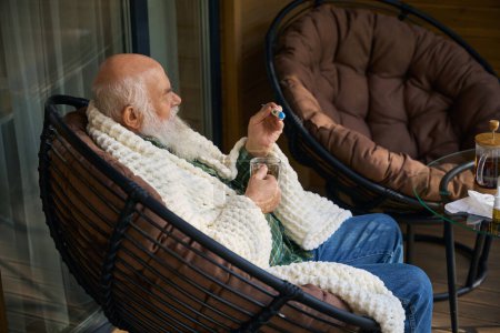 Foto de Pensionista con un té frío en la terraza, tiene un termómetro en sus manos - Imagen libre de derechos