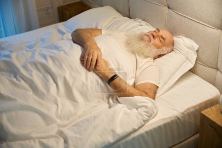 Photo for Old man sleeps on his back in comfortable bed, with a glass of water on the nightstand next to him - Royalty Free Image