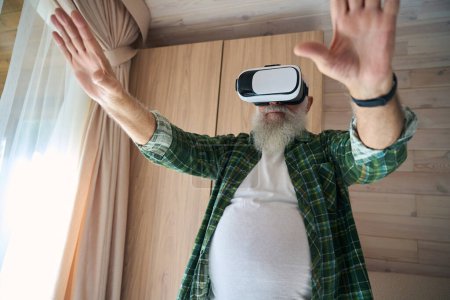 Téléchargez les photos : Homme âgé portant des lunettes de réalité virtuelle, il joue dans une salle lumineuse confortable - en image libre de droit