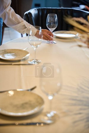 Foto de Camarera en una chaqueta blanca sirve una mesa en una sala de restaurante, hay un mantel blanco en la mesa - Imagen libre de derechos