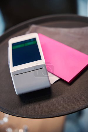 Téléchargez les photos : Terminal pour les clients payants et une enveloppe rose avec une facture sur un plateau brun - en image libre de droit