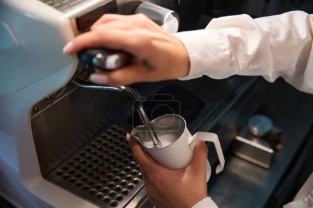 Téléchargez les photos : Barista en chemisier blanc fait mousser le lait dans une machine à café, équipement moderne est utilisé - en image libre de droit