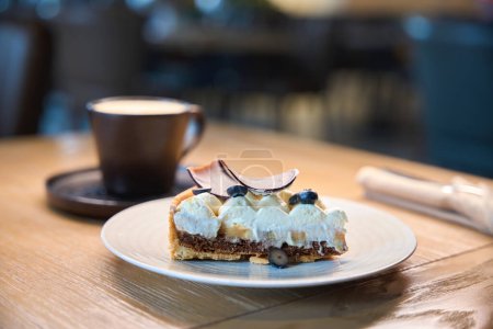 Foto de Taza de café y un platillo con un pastel están sobre la mesa, el pastel está decorado con bayas frescas - Imagen libre de derechos