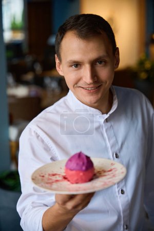 Téléchargez les photos : Chef présente un dessert spectaculaire, un gâteau rose repose sur une assiette minimaliste - en image libre de droit