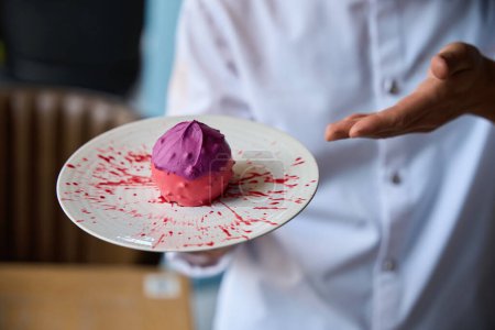 Téléchargez les photos : Chef pâtissier présente un dessert aux fruits original, un gâteau rose repose sur une assiette minimaliste - en image libre de droit