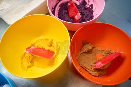 Photo for Top view of three bowls with colored batter and silicone spatulas on kitchen countertop - Royalty Free Image