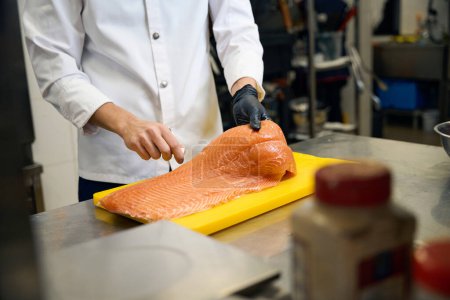 Téléchargez les photos : Chef coupe du poisson rouge avec un couteau tranchant, il travaille sur une grande planche à découper jaune - en image libre de droit