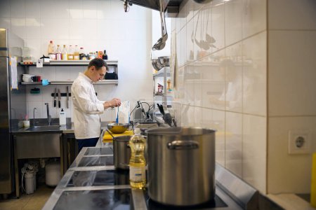 Téléchargez les photos : Jeune homme casse des œufs dans un bol, il prépare la nourriture dans une cuisine de restaurant - en image libre de droit