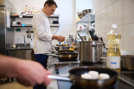 Photo for Young chef is preparing food in a restaurant kitchen, he is in a comfortable uniform - Royalty Free Image