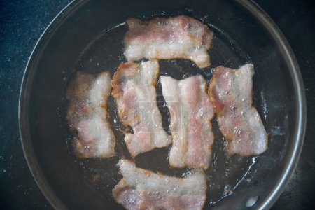 Téléchargez les photos : Le bacon de haute qualité est frit dans une poêle à frire à l'aide d'une cuisinière moderne - en image libre de droit