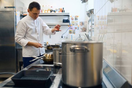 Foto de El tipo de uniforme prepara comida en la cocina de un restaurante, usa especias - Imagen libre de derechos