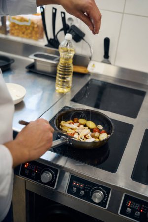 Foto de Chef sal verduras en una sartén, aceite vegetal está cerca - Imagen libre de derechos
