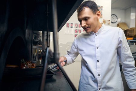 Foto de Joven chef saca una sartén con carne del horno, utiliza productos de calidad - Imagen libre de derechos