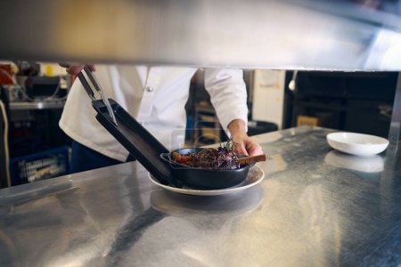 Foto de Cook pone una sartén de servir con carne en un plato, utiliza productos de calidad - Imagen libre de derechos