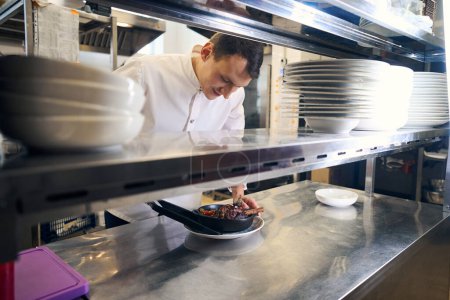 Téléchargez les photos : Employé de cuisine a préparé la tige d'agneau avec des légumes pour servir, il prépare la nourriture dans la cuisine du restaurant - en image libre de droit
