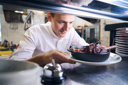 Photo for Young man has prepared lamb shank with vegetables for serving, he is preparing food in the restaurant kitchen - Royalty Free Image