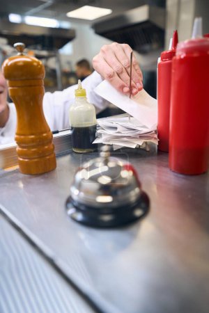 Foto de La campana de metal está en un estante en la cocina de un restaurante, un empleado está grabando un recibo de ventas - Imagen libre de derechos