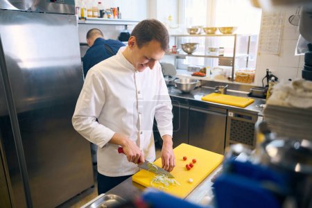 Foto de El personal de la cocina corta verduras en una tabla de cortar amarilla, usa un cuchillo afilado - Imagen libre de derechos