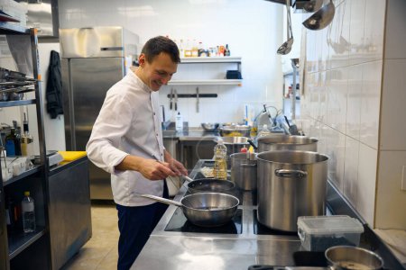 Téléchargez les photos : Jeune chef cuisinier sur une poêle, il utilise un équipement professionnel - en image libre de droit