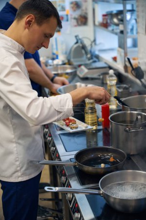 Foto de El empleado de cocina cocina cocina en una sartén, utiliza equipo profesional - Imagen libre de derechos