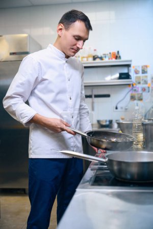 Foto de Chef cocina en una sartén, utiliza equipo profesional - Imagen libre de derechos