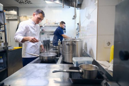 Téléchargez les photos : Cuisinier prépare des pâtes noires dans une poêle, il utilise un équipement professionnel - en image libre de droit