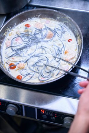 Foto de Chico cocina espaguetis negros en salsa, utiliza productos de alta calidad - Imagen libre de derechos