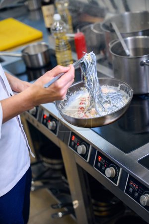 Téléchargez les photos : Chef prépare des spaghettis noirs dans une sauce spéciale, il utilise des produits de haute qualité - en image libre de droit