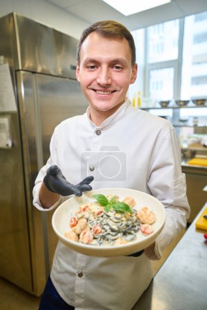Foto de Chef presenta espaguetis en una salsa especial, trabaja con guantes protectores - Imagen libre de derechos