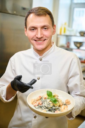 Foto de Chef presenta espaguetis negros en una salsa especial, trabaja con guantes protectores - Imagen libre de derechos